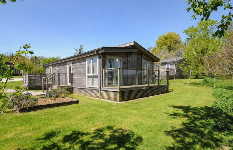 A wooden cabin with a glass railing on a deck surrounded by grass and trees at 19 Meadow Retreat in Dobwalls