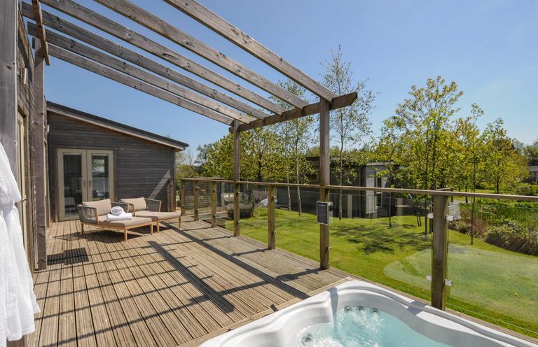 A wooden deck with a hot tub a lounge chair and a wooden pergola overlooking a garden at 11 Meadow Retreat in Dobwalls