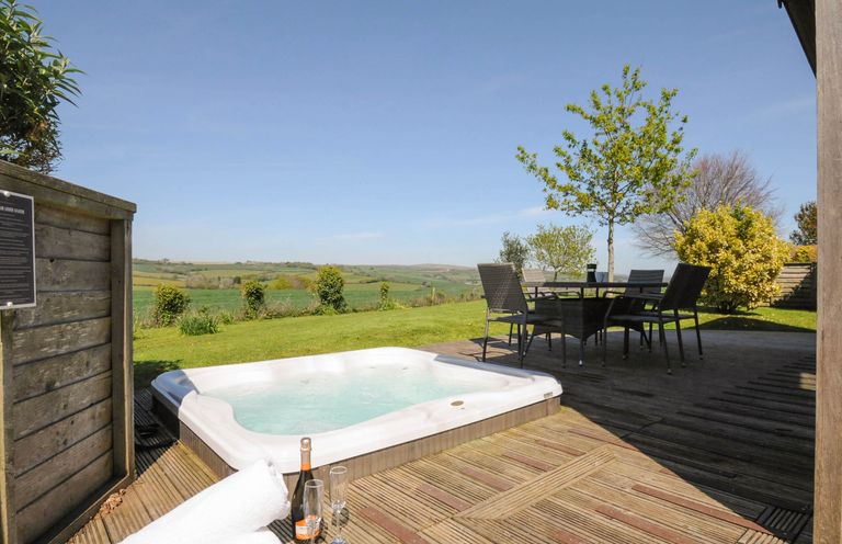 An outdoor deck with a hot tub table with chairs towels a bottle and glasses overlooking fields at 4 Horizon View in Dobwalls