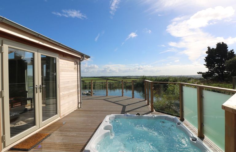 An outdoor deck with a hot tub and glass railing overlooking a body of water at 14 Faraway Fields in Dobwalls