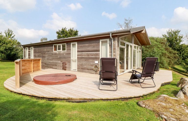 A wooden cabin with large windows and two black chairs on a wooden deck in a grassy area at 11 Horizon View in Dobwalls