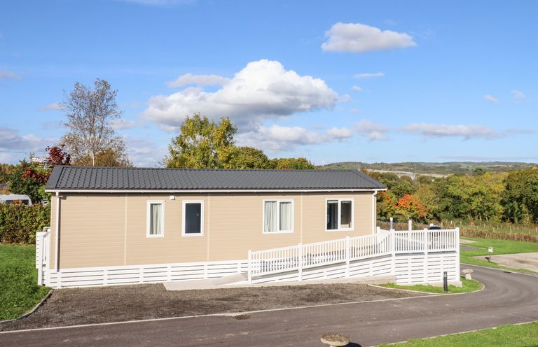 A beige mobile home with white railing and ramp surrounded by green grass and trees at Chestnut Lodge in Teigngrace near Newton Abbot