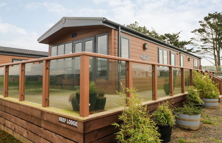 An exterior view of a wooden lodge with glass railing and potted plants outside at Reef Retreat in Broad Haven