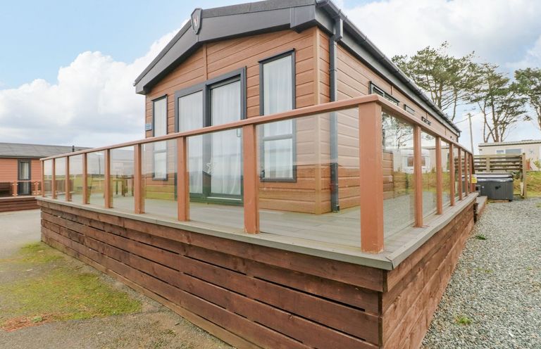 A wooden cabin with glass railing on a deck surrounded by gravel and grass at Seahorse Retreat in Little Haven near Broad Haven