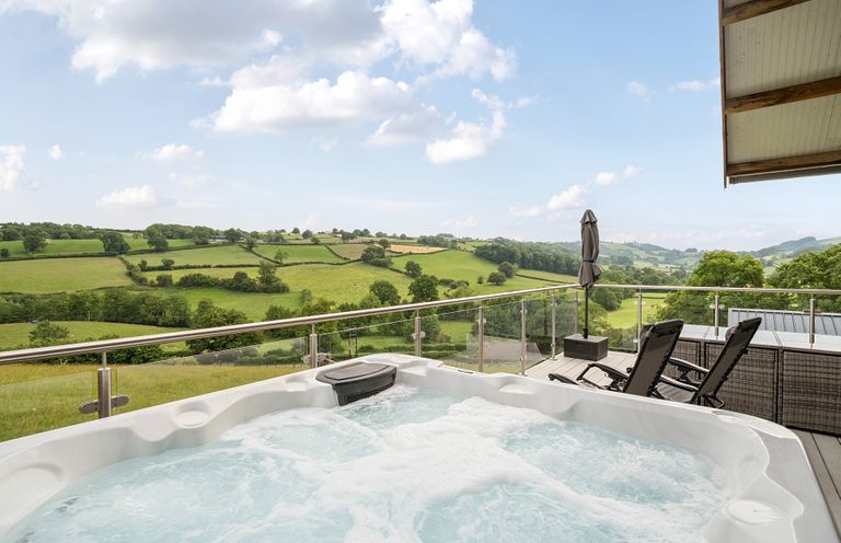An outdoor area with a hot tub and chairs overlooking the countryside at Bwncath in Garthmyl