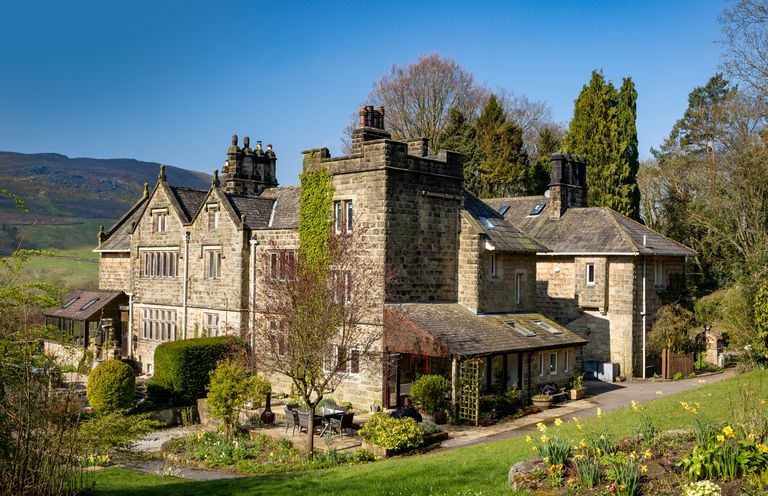 A stone house with chimneys surrounded by garden and trees at Kail House in Grassington