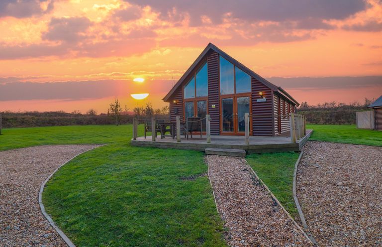 A cabin with a deck and chairs during sunset at Lodge 3 Thorpe-On-The-Hill