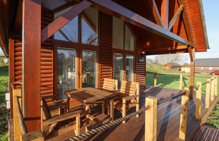 A wooden porch with a table and chairs outside a log cabin at Lodge 7 in South Hykeham