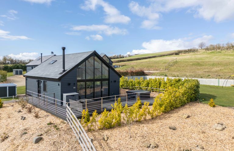 A modern house with large glass windows and a fenced garden surrounded by grassy hills at Stags Mount in Thornton Dale