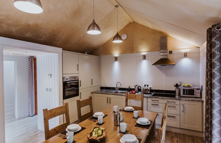 A kitchen with wooden chairs around a table set with white bowls and mugs at Lodge 8 in Corfe Castle