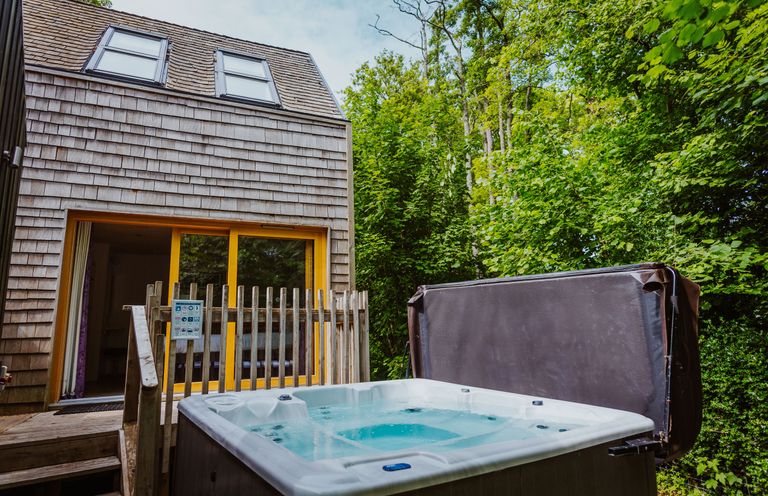 An outdoor hot tub next to a wooden house with sliding glass doors surrounded by trees at Lodge 17 in Corfe Castle
