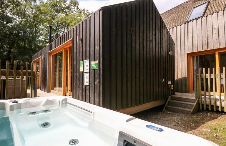 An outdoor hot tub next to a modern wooden cabin with sliding glass doors at Lodge 22 in Corfe Castle