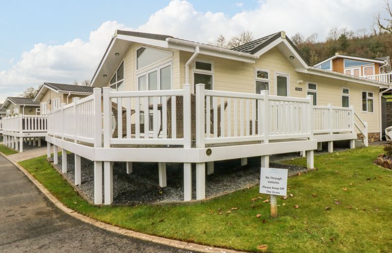 A beige lodge with white railings on a raised deck and grass around at Dono's Lodge Stepaside near Kilgetty Heritage Park