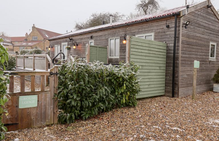 A wooden lodge with a gravel driveway bushes and wooden gates at Grouse Lodge in Seamer North Yorkshire