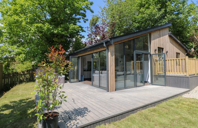 A wooden cabin with large glass doors opening onto a deck surrounded by trees at The Nest Brython in Tenby