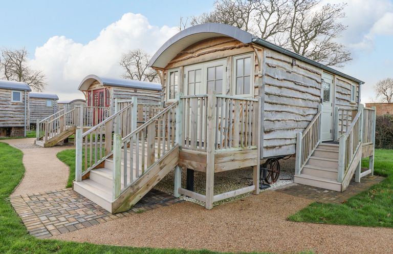 A group of wooden shepherd huts with stairs and railings on a grassy area at Folklore in Bolton Percy near Tadcaster