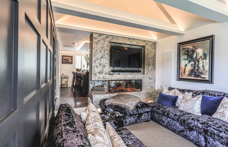 A living room with a sectional sofa and pillows a fireplace with a mounted TV and a painting on the wall at Whisk Away Cottage in Greystoke near Troutbeck Near Penrith