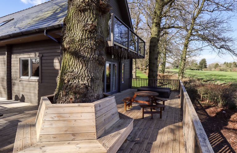 A wooden deck with built-in seating around a large tree and outdoor furniture at iLodge Ultra in Kenwick near Louth