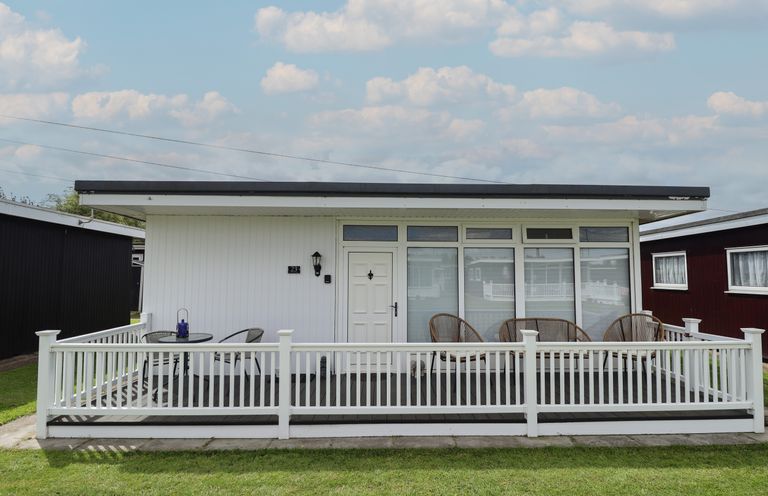 A small white house with a porch and outdoor furniture at 23 Cherry Park in Chapel St Leonards