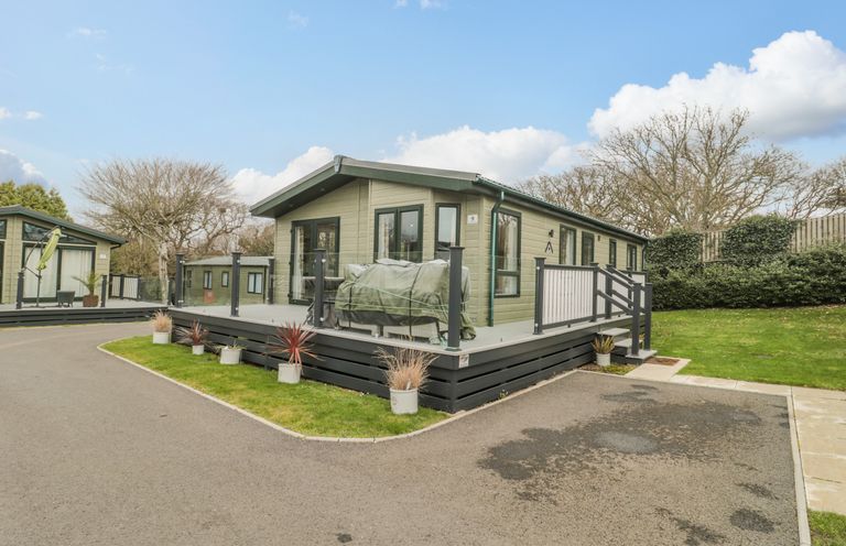 A green lodge with a raised deck and potted plants beside a paved driveway at Gwydn Lodge in Downton Hampshire