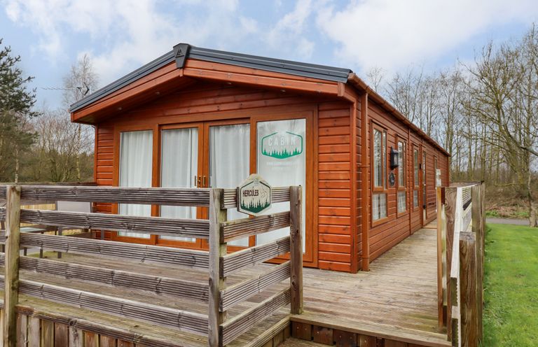 A wooden cabin with glass doors and windows and a wooden deck at Hercules in Felmoor Park