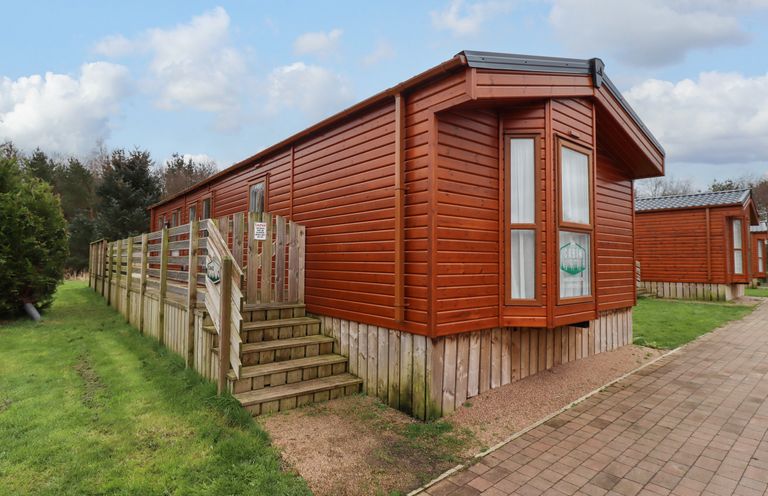 An outdoor view of a wooden cabin with a small staircase and a fenced porch at Canis in Felmoor Park