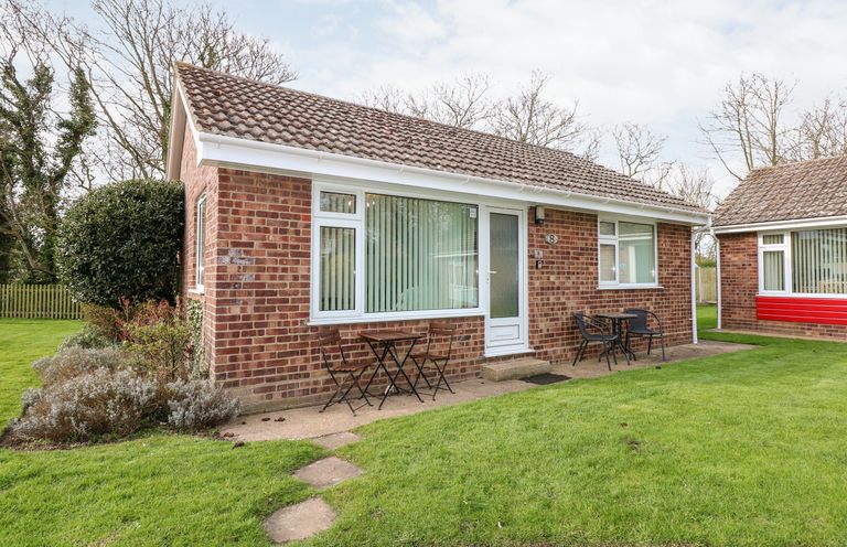 A brick single-story house with two outdoor seating areas and grass lawn at 8 Royal Chalet Park in Mundesley