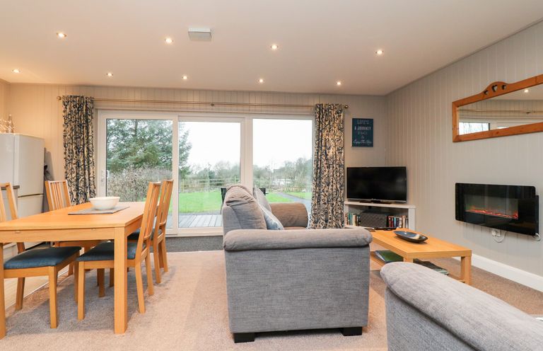 A living room with grey sofas a wooden dining table and chairs a television and sliding glass doors at Beech Lodge in Goosnargh