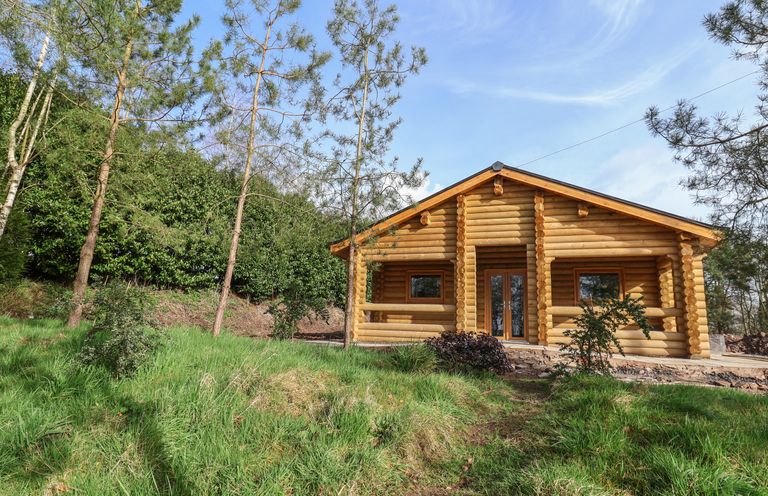 A wooden log cabin surrounded by trees and grass at Redwood Lodge in Ellesmere