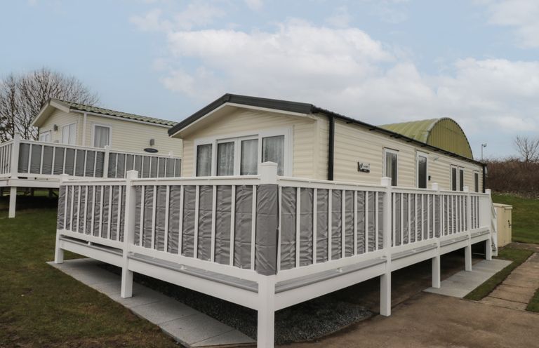 A mobile home with a white railing and a paved pathway at Rowan Court 2 in Cayton