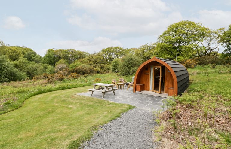 A wooden pod with patio furniture on a stone terrace surrounded by grass and trees at Llugwy Pod in Capel Garmon near Betws-Y-Coed