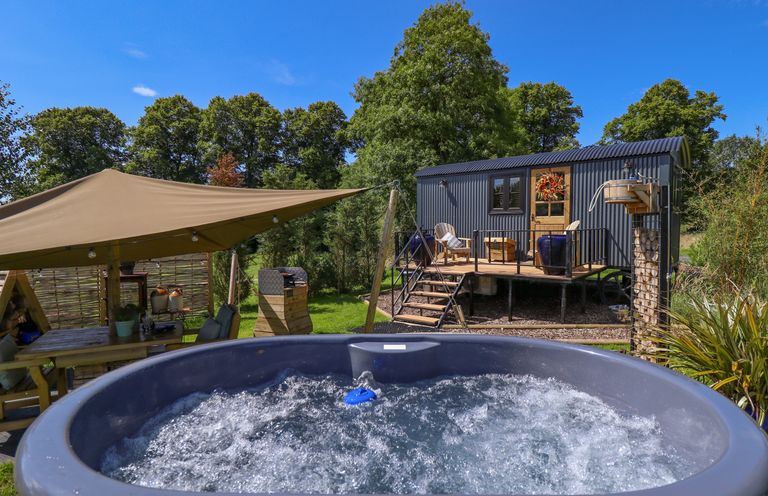 A hot tub in front of a wooden cabin with outdoor seating and a canopy at Portland Luxury Glamping in Nottingham
