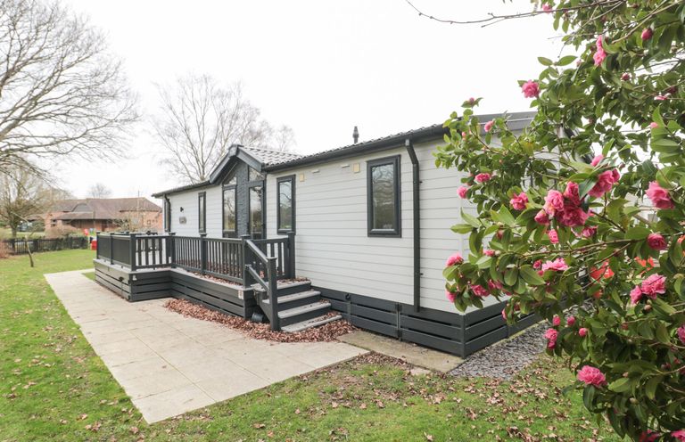 A white and gray prefab house with a small porch and steps surrounded by grass and pink flowers at Owls Nest in Furzehill