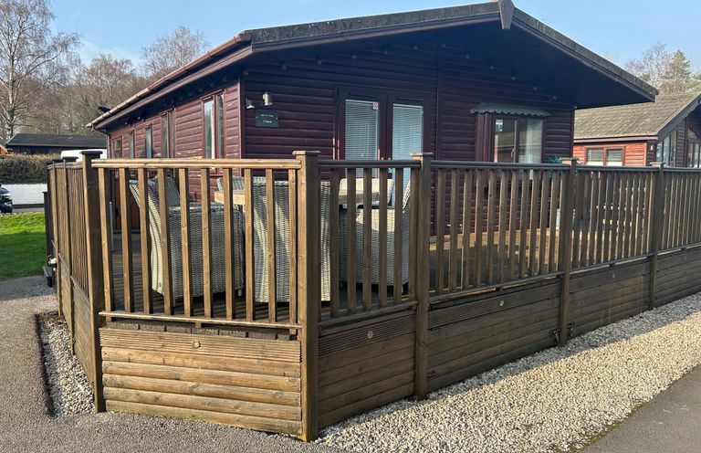 A wooden cabin with a deck and fence at Lake View Lodge, Lakeside 3, White Cross Bay, Windermere