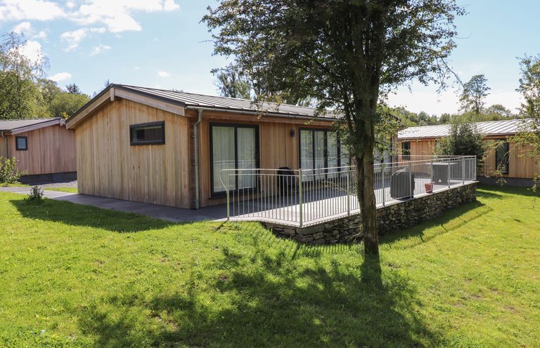 A wooden cabin with a metal roof and a patio area surrounded by a railing on grass at Hawthorn Croft in Haverthwaite