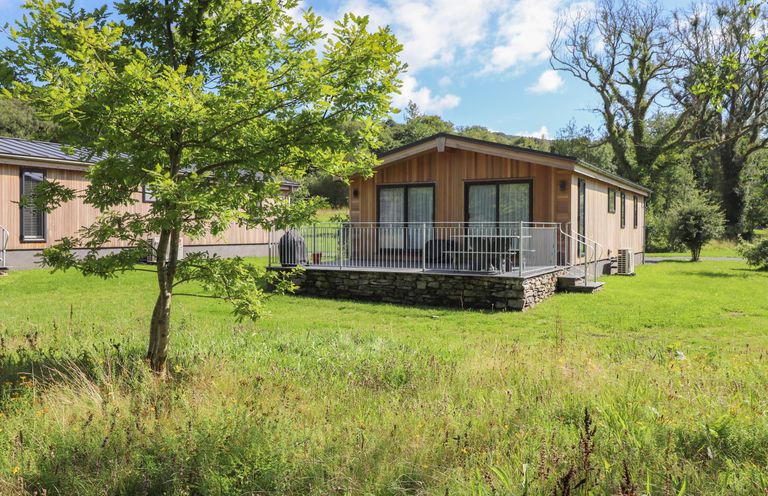 A wooden cabin with patio and railing surrounded by grass and trees at The Brambles in Haverthwaite