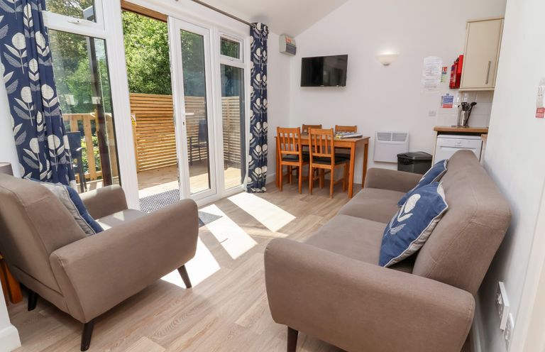 A living area with two armchairs and a sofa near glass doors and a dining table with four chairs at Chalet Log Cabin C9 in Combe Martin
