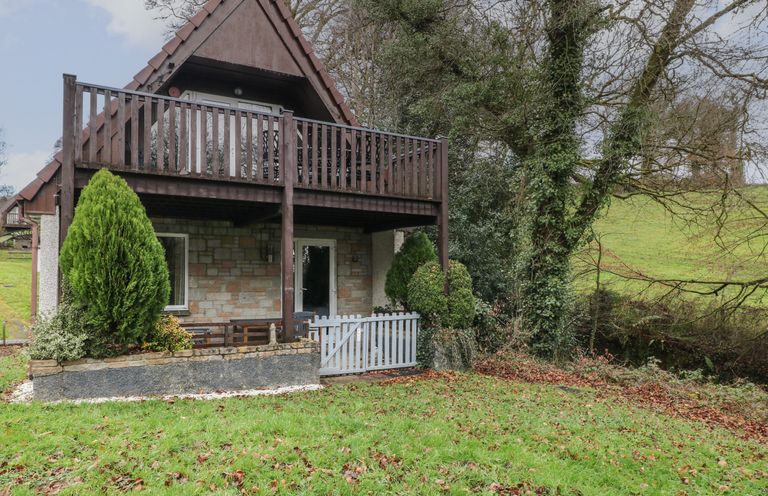 A two-story house with a stone lower floor and wooden balcony surrounded by grass and trees at Valley Lodge 55 Callington near Gunnislake