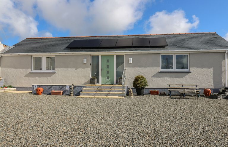 A single story house with a green door solar panels on the roof and gravel in front at Brynteg Cottage in Tegryn