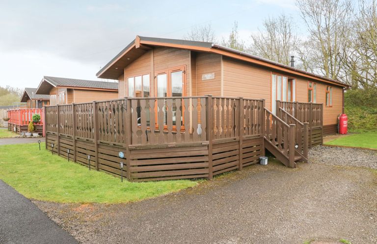 A brown wooden cabin with a fenced deck and steps on a grassy plot at Walkers Rest in Warton near Carnforth