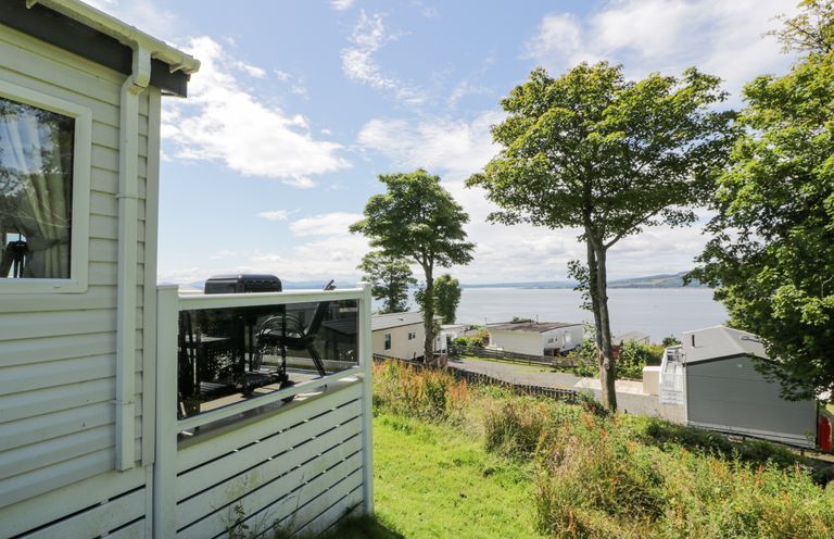 A view of a grassy hillside with trees and several mobile homes overlooking a body of water at Olivias Haven in Wemyss Bay