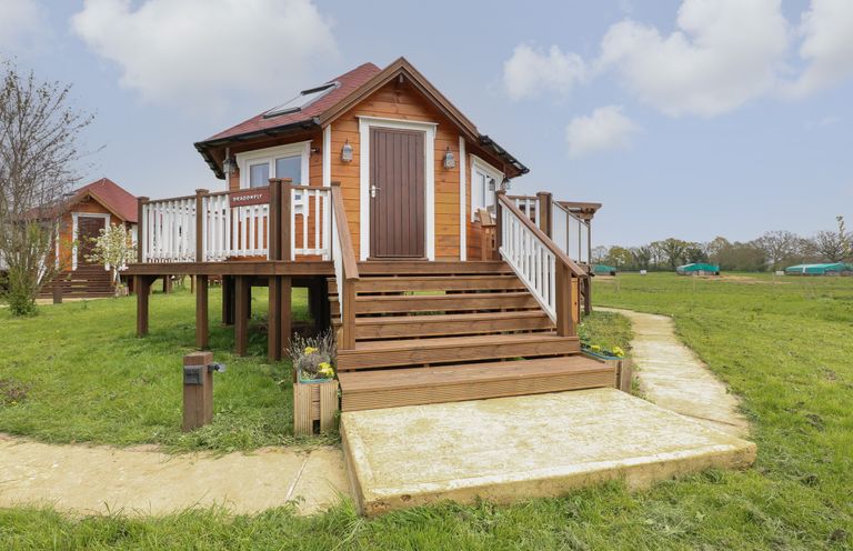A wooden cabin elevated with stairs and railings on a grassy field at Dragonfly Retreat in Upper Marham