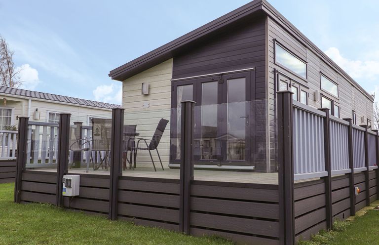 A modern exterior of a lodge with glass and wood railing on a raised deck with outdoor chairs and table at Tiptoes Lodge in Carnforth