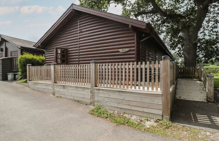 A wooden cabin with a fenced porch and a ramp leading to the entrance at Oaks in Swanage