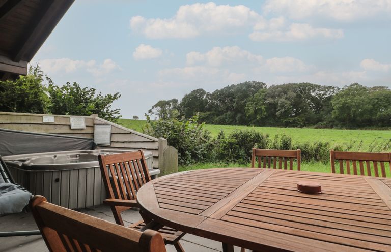 An outdoor patio with a wooden table and chairs next to a hot tub overlooking a green field at Walnut in Swanage
