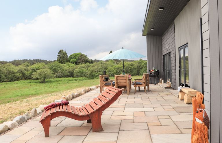 An outdoor patio with wooden lounge chair table and chairs with umbrella and a carved wooden bird Pine Marten Dornoch