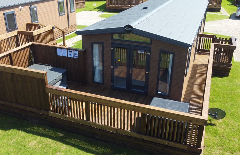 A wooden cabin with a fenced deck and outdoor seating at Honeysuckle Lodge in Runswick Bay near Staithes
