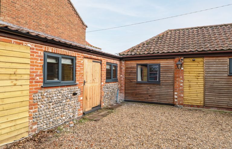 The exterior courtyard of a building with gravel ground brick and wooden walls and windows at Squirrel Lodge in North Walsham