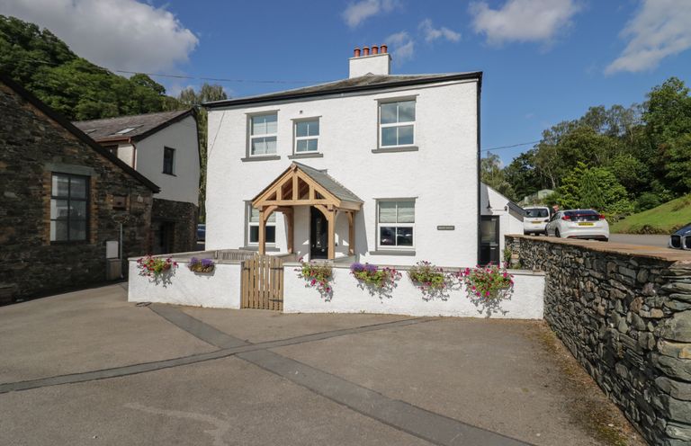 A white two-story house with a wooden porch and flower boxes in front surrounded by a stone wall at Briery House in Keswick