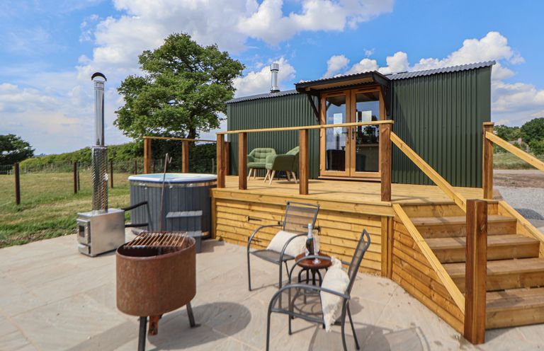 An outdoor patio with chairs a fire pit hot tub and a wooden deck at The Coop in Aston near Woore
